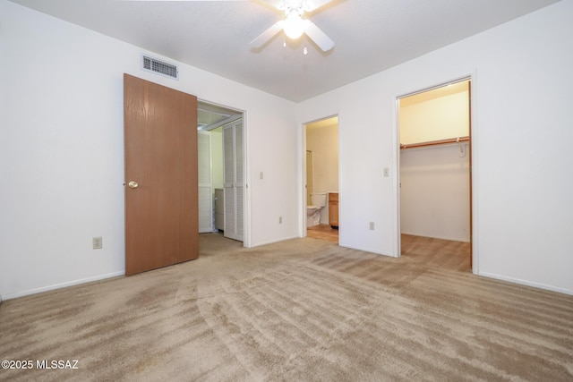 unfurnished bedroom featuring ensuite bathroom, a walk in closet, light carpet, a closet, and ceiling fan