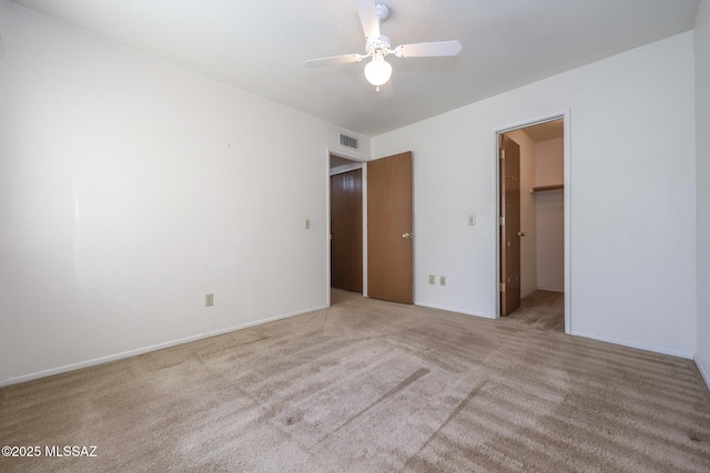 unfurnished bedroom with ceiling fan, a walk in closet, light colored carpet, and a closet