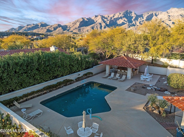 pool at dusk featuring a mountain view, a patio area, and exterior bar