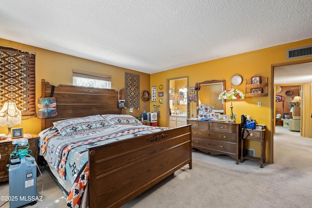 bedroom with ensuite bath, a textured ceiling, and light carpet