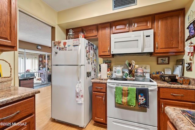 kitchen with white appliances, a textured ceiling, and light hardwood / wood-style flooring