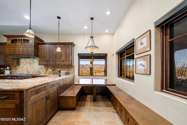 kitchen featuring light stone counters, decorative light fixtures, sink, and backsplash