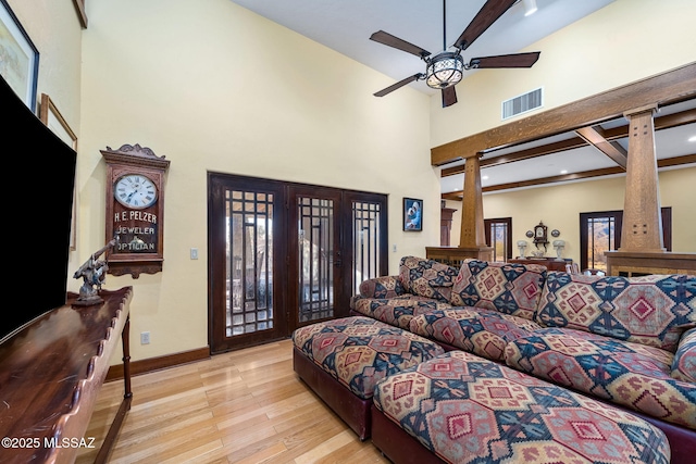 living room featuring a towering ceiling, beamed ceiling, ceiling fan, and light wood-type flooring