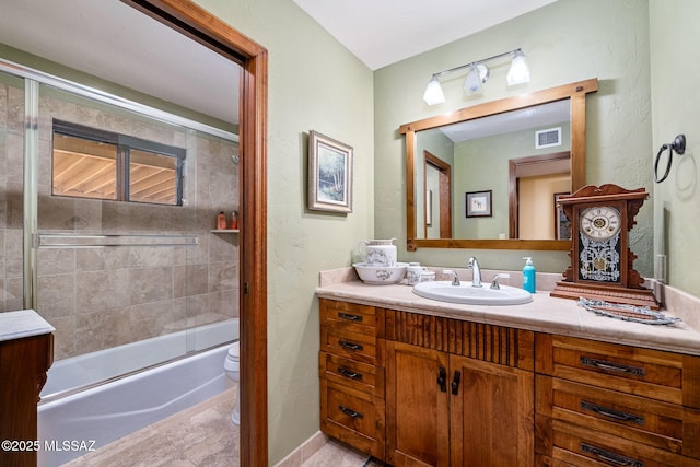 full bathroom with bath / shower combo with glass door, vanity, and toilet