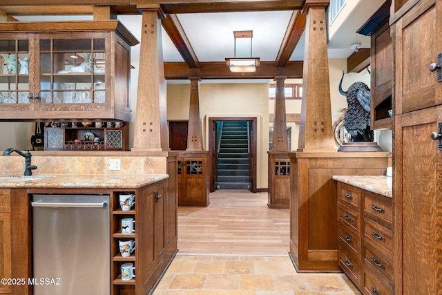 kitchen with sink, ornate columns, light stone counters, stainless steel dishwasher, and beam ceiling