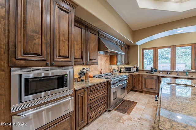 kitchen with appliances with stainless steel finishes, ventilation hood, light stone counters, decorative backsplash, and sink