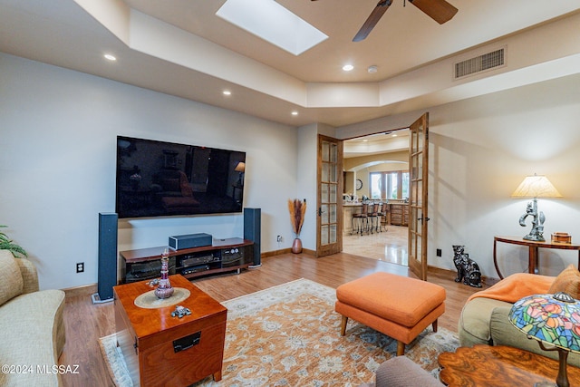 living room with french doors, a skylight, ceiling fan, and light hardwood / wood-style flooring