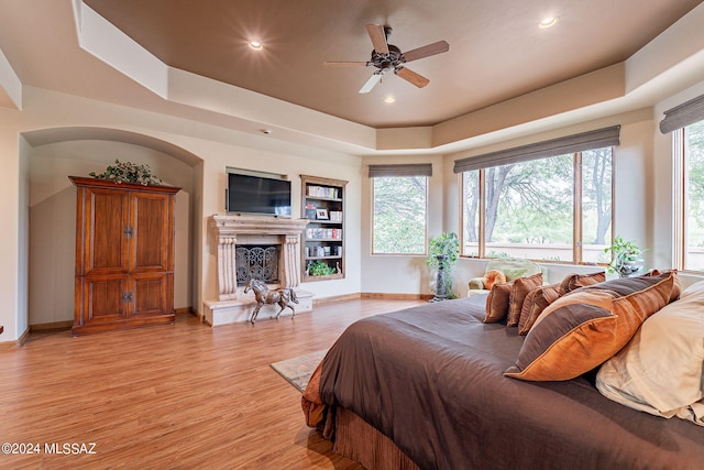 bedroom with ceiling fan, light wood-type flooring, and a tray ceiling