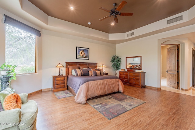 bedroom with ceiling fan, light wood-type flooring, and a raised ceiling