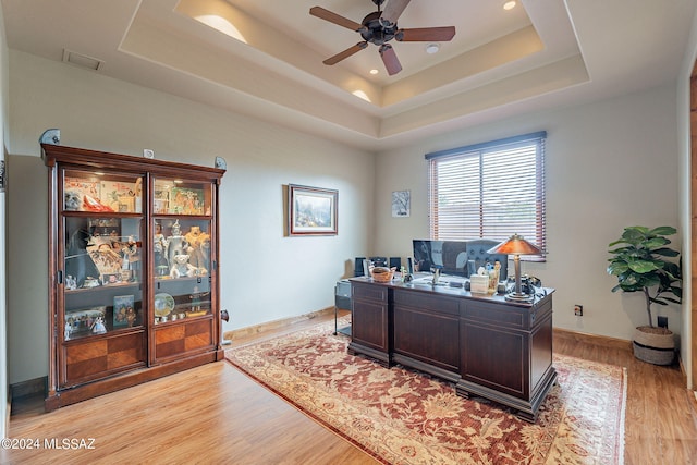 office space with a raised ceiling, ceiling fan, and light hardwood / wood-style flooring