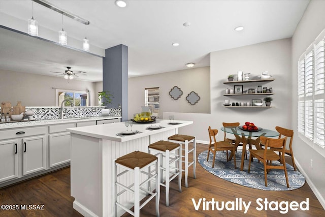 kitchen featuring a breakfast bar area, hanging light fixtures, ceiling fan, dark wood-type flooring, and a kitchen island