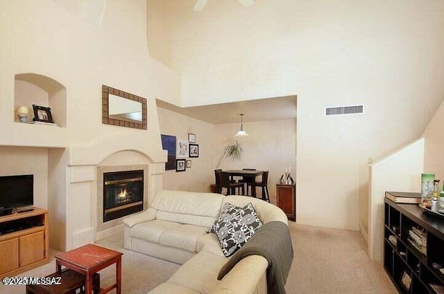 living room with ceiling fan, light carpet, and a towering ceiling