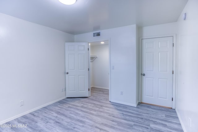 unfurnished bedroom featuring a closet, a walk in closet, and light hardwood / wood-style flooring