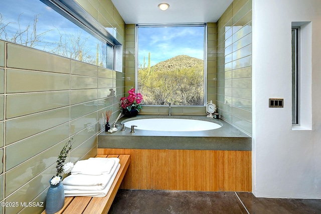 bathroom with concrete flooring, a garden tub, a mountain view, and tile walls