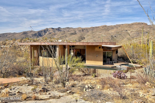 exterior space with a pool with connected hot tub, a mountain view, and stucco siding