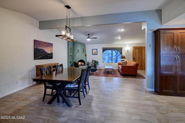 dining area with lofted ceiling with beams, a large fireplace, and ceiling fan with notable chandelier