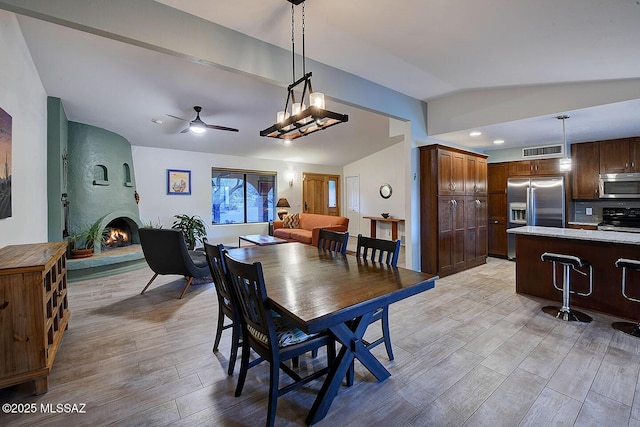 dining space with ceiling fan, lofted ceiling, a large fireplace, and light wood-type flooring