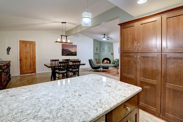 kitchen featuring pendant lighting, ceiling fan, light stone counters, light hardwood / wood-style floors, and vaulted ceiling