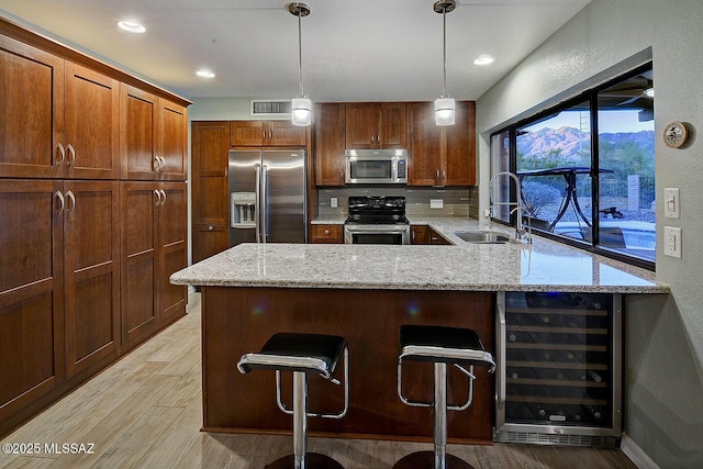 kitchen with appliances with stainless steel finishes, sink, wine cooler, a kitchen breakfast bar, and light stone countertops