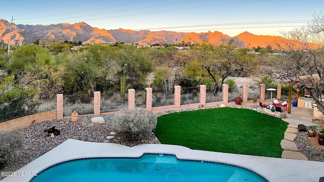 pool at dusk with a yard, a mountain view, and a patio