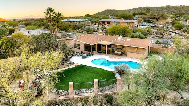 pool at dusk with a patio and a lawn