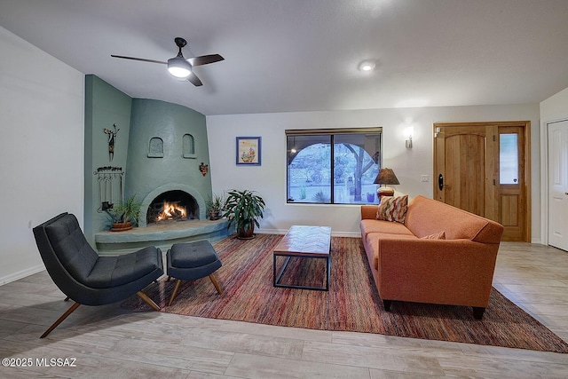 living room with ceiling fan, a large fireplace, and light hardwood / wood-style floors