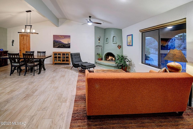 living room with vaulted ceiling with beams, ceiling fan with notable chandelier, wood-type flooring, and a large fireplace