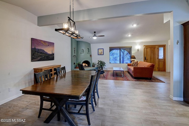 dining area with beam ceiling, a fireplace, ceiling fan, and light wood-type flooring