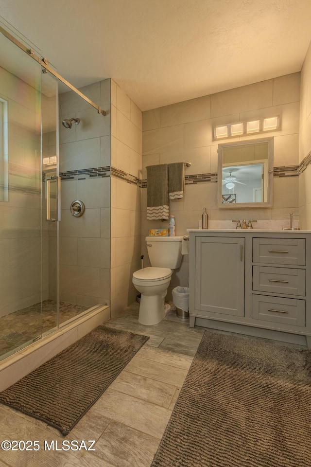 bathroom with toilet, walk in shower, vanity, tile walls, and ceiling fan