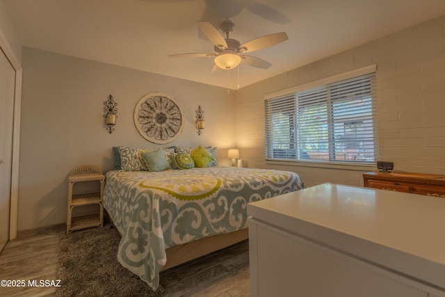 bedroom featuring ceiling fan, hardwood / wood-style floors, and brick wall