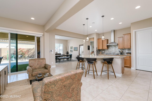 kitchen featuring tasteful backsplash, recessed lighting, a breakfast bar, an island with sink, and wall chimney range hood