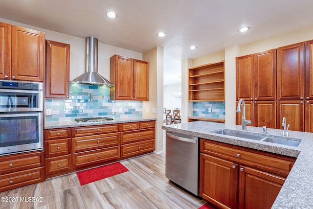 kitchen featuring wall chimney range hood, sink, stainless steel appliances, tasteful backsplash, and light stone counters