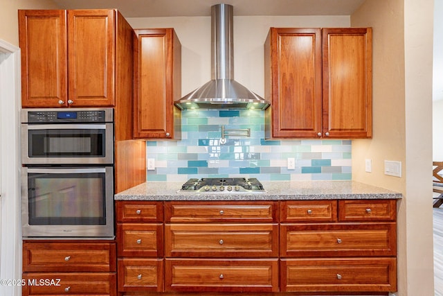 kitchen featuring light stone counters, appliances with stainless steel finishes, decorative backsplash, and wall chimney range hood