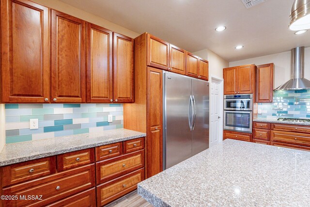 kitchen featuring light stone countertops, appliances with stainless steel finishes, wall chimney range hood, and decorative backsplash