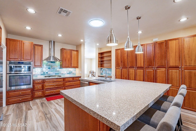 kitchen with sink, decorative light fixtures, a large island with sink, appliances with stainless steel finishes, and wall chimney range hood