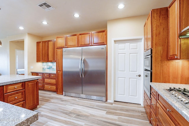 kitchen with light stone counters, decorative backsplash, and stainless steel appliances