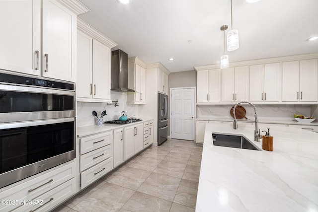 kitchen featuring appliances with stainless steel finishes, decorative light fixtures, white cabinetry, sink, and wall chimney range hood