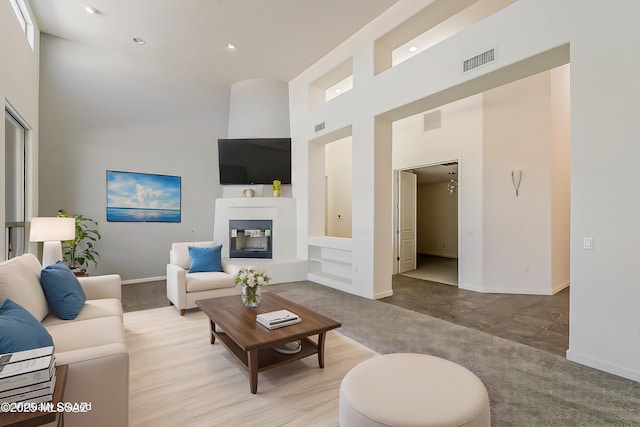 carpeted living area with visible vents, baseboards, recessed lighting, a towering ceiling, and a glass covered fireplace