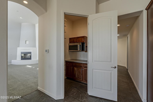 hallway featuring arched walkways, baseboards, and dark colored carpet