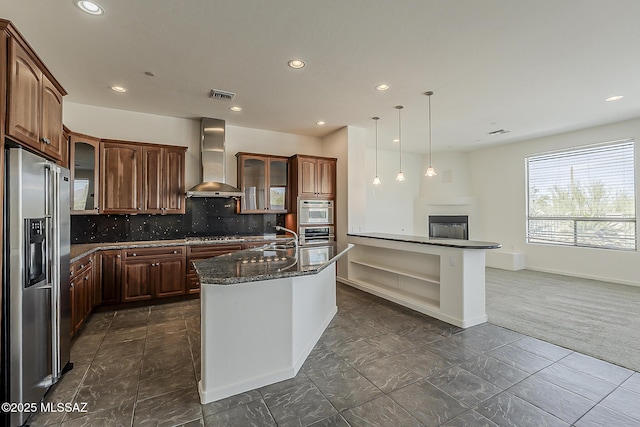 kitchen with tasteful backsplash, visible vents, glass insert cabinets, wall chimney range hood, and stainless steel appliances