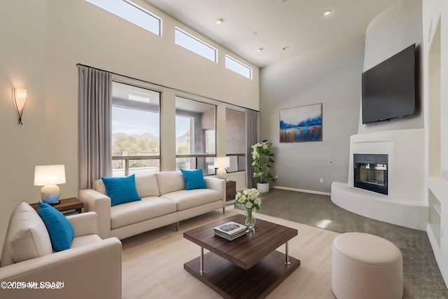 living room featuring a glass covered fireplace, a high ceiling, and baseboards