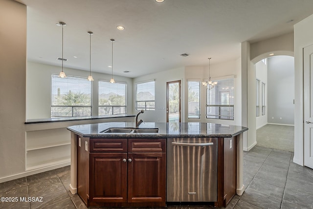 kitchen with a sink, dark stone counters, arched walkways, and an island with sink