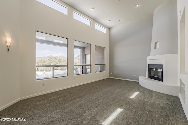 unfurnished living room with a glass covered fireplace, a towering ceiling, baseboards, and dark colored carpet