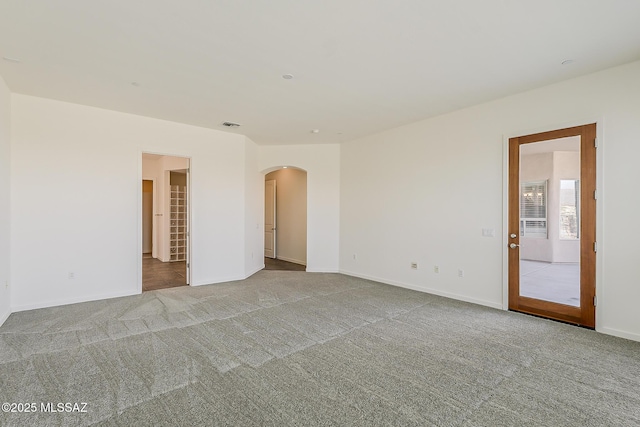 carpeted empty room with baseboards, arched walkways, and visible vents