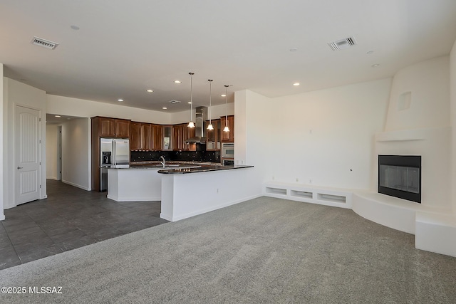 kitchen with dark countertops, visible vents, stainless steel fridge, and ventilation hood