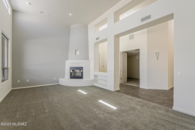 unfurnished living room featuring visible vents, carpet floors, a towering ceiling, and a glass covered fireplace