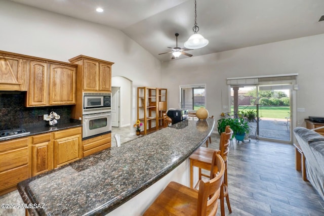 kitchen with appliances with stainless steel finishes, pendant lighting, a breakfast bar area, backsplash, and hardwood / wood-style flooring