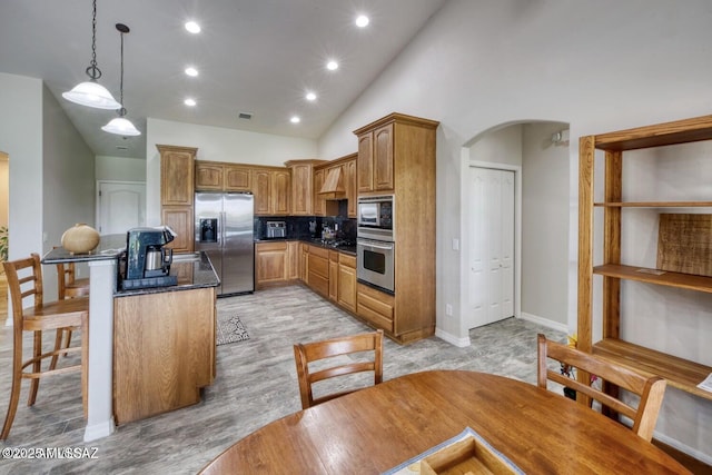 kitchen featuring a breakfast bar, high vaulted ceiling, decorative light fixtures, tasteful backsplash, and stainless steel appliances