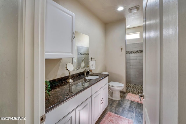 bathroom with vanity, wood-type flooring, toilet, and tiled shower