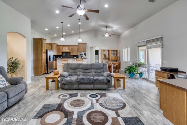 living room with a towering ceiling, ceiling fan, and light wood-type flooring